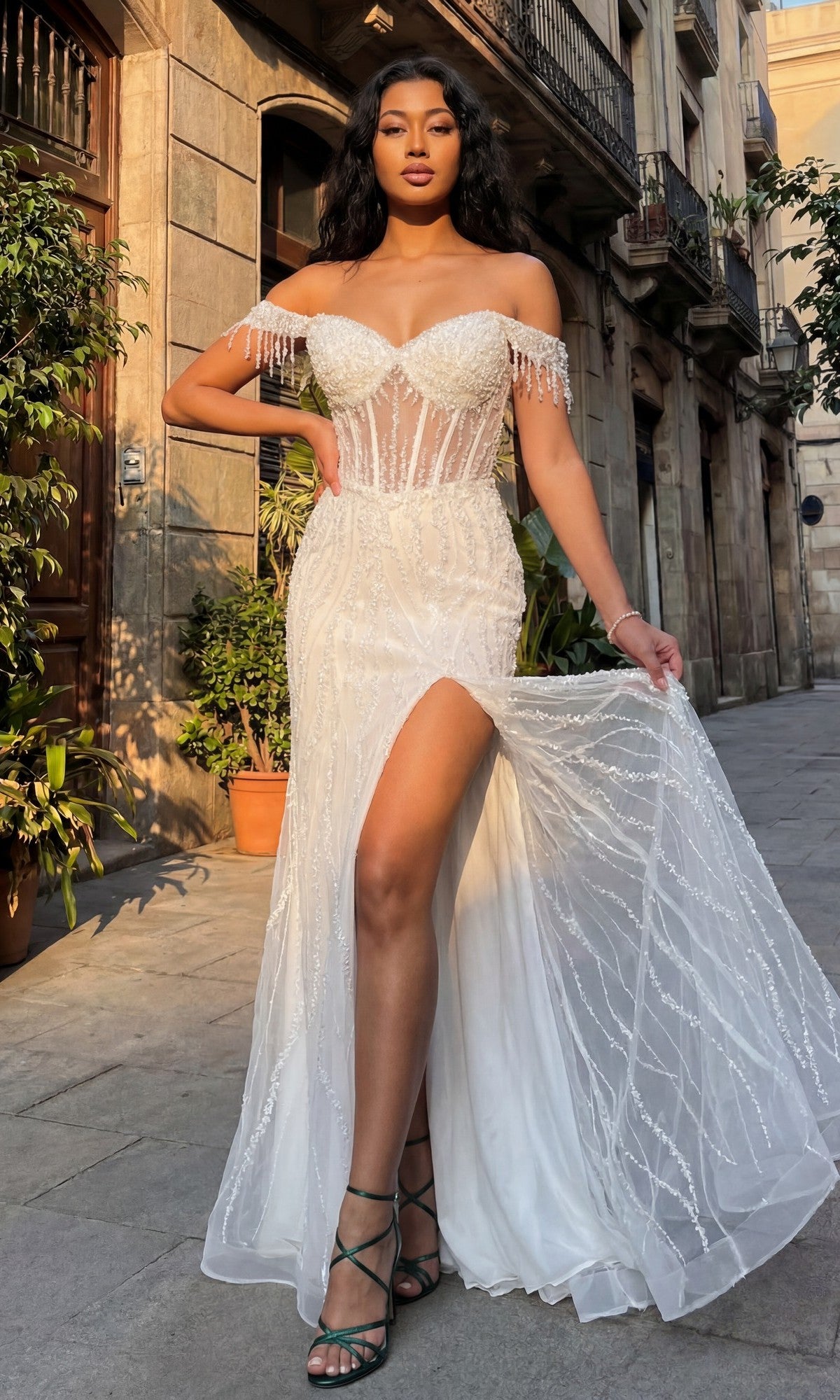 A woman poses outdoors on a city street wearing the Chicas C331 Off-Shoulder Long Sequin Prom Dress, featuring a white beaded design, high slit, and transparent corset bodice.